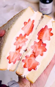 Hands holding a whipped cream fruit sandwich that's been halved with flower strawberry cutouts