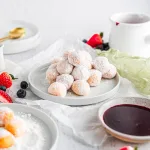 donuts stacked in a pyramid on a white plate with assorted berries and dipping sauce