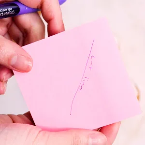 Sticky note being held by hands with a line and hand written note saying 'cut line'