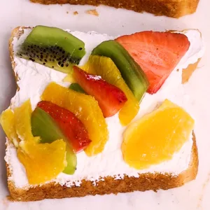 An opened sandwich showing the inside with whipped cream and strawberry, kiwi, and orange pattern laid out on top of whipped cream on sandwich.