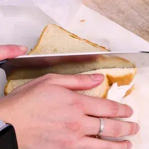 Whipped cream fruit sandwich being cut in half with a sharp knife