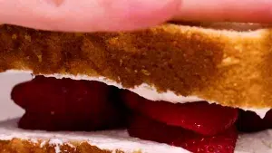 Close up of fruit sandwich with whipped cream being closed by hand.