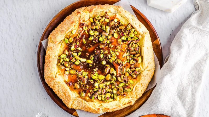 Galette made with flakey crust, sweet cheese filling and pistachios topped on a wooden serving dish and on a neutral background