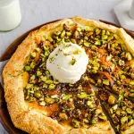 Galette made with flakey crust, sweet cheese filling and pistachios topped with ice cream on a wooden plate