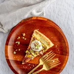 Galette made with flakey crust, sweet cheese filling and pistachios topped with ice cream on a wooden plate with two gold forks