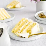 White yuzu cake with yellow yuzu filling frosted with vanilla frosting, sliced on white plate on neutral background