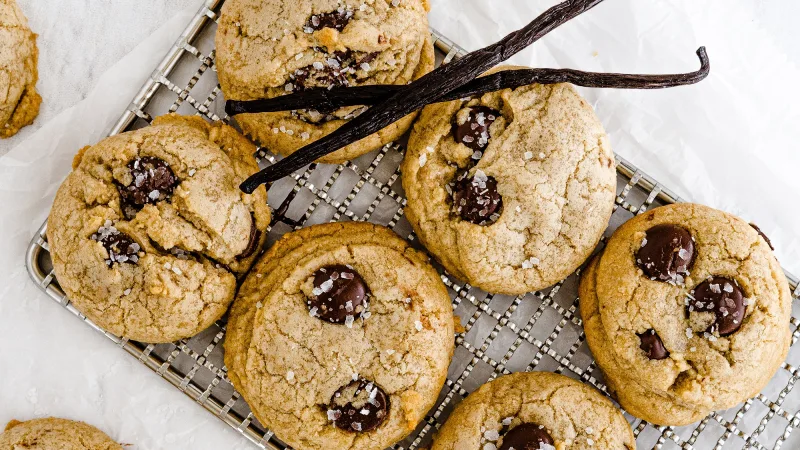 Carmel brown colored chocolate chip cookies on cooling rack with vanilla beans and vanilla extract