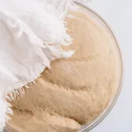 top shot of the star bread dough in a glass bowl. A white kitchen towel lays over a section of the bowl.