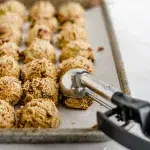 Close up of a cookie scooper and tray with a bunch of halva cookie dough balls.