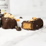 side close up shot of a cut chocolate peanut butter bar laying on parchment paper. In the background is a bottle of Rodelle Madagascar Pure Vanilla Extract.