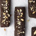 Top view of rectangular chocolate covered peanut butter bars laying on top of parchment paper. Spinkled on top of the candy bars and scattered around the scene are crushed peanuts.