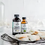 Landscape photo of a bundle of Vanilla Peppermint Shortbread dipped in White Chocolate round cookies laying on a white with brown speckled plate. Surrounding the cookies is a gray kitchen cloth. Next to the cookies is Rodelle's Pure Madagascar Bourbon Vanilla Extract and Rodelle Peppermint Extract.