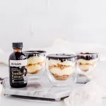 side profile of three eclair cake parfaits on a decorative gray marble board with Rodelle 2oz FairTrade Vanilla Extract right next to the parfaits.