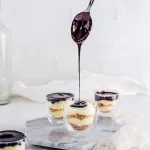 A spoon drizzling chocolate syrup on top of an eclair parfait.