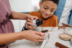 Child pouring Rodelle vanilla paste into a tablespoon with help of mother holding childs hand.