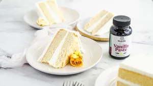 Vanilla cake on a plate with a yellow flower with a vanilla paste bottle next to it.