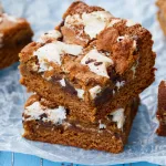 close up of s'mores bar sliced on parchment paper on blue background