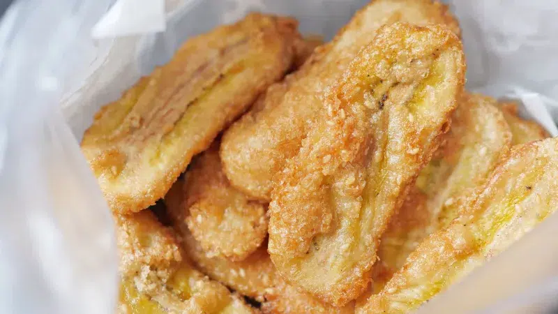 Close up of a batch of banana fritters sliced length wise and in half laying in parchment paper.